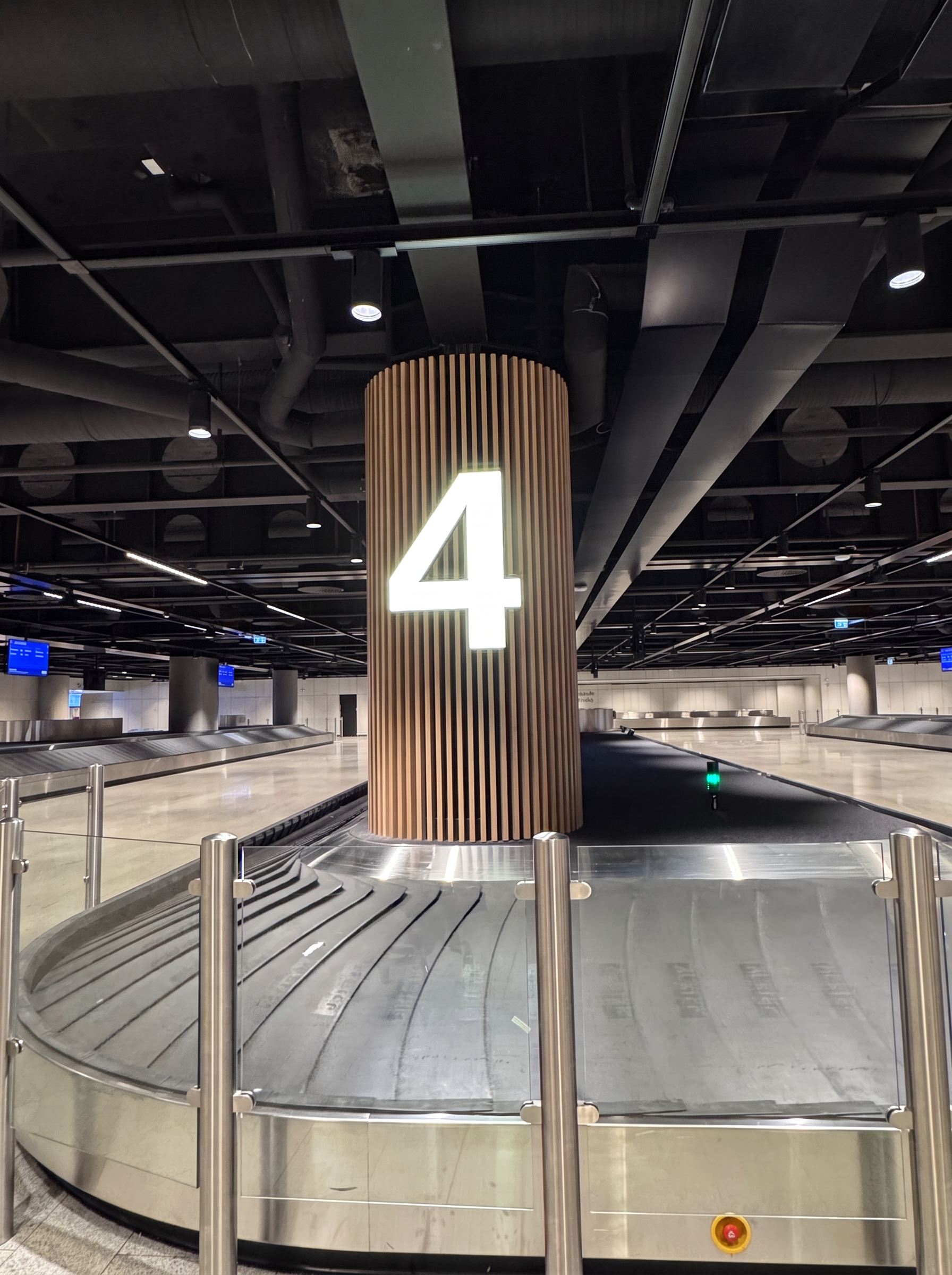 Baggage reclaim hall at Keflavík Airport with a large lit number four above a luggage belt and screens along the wall